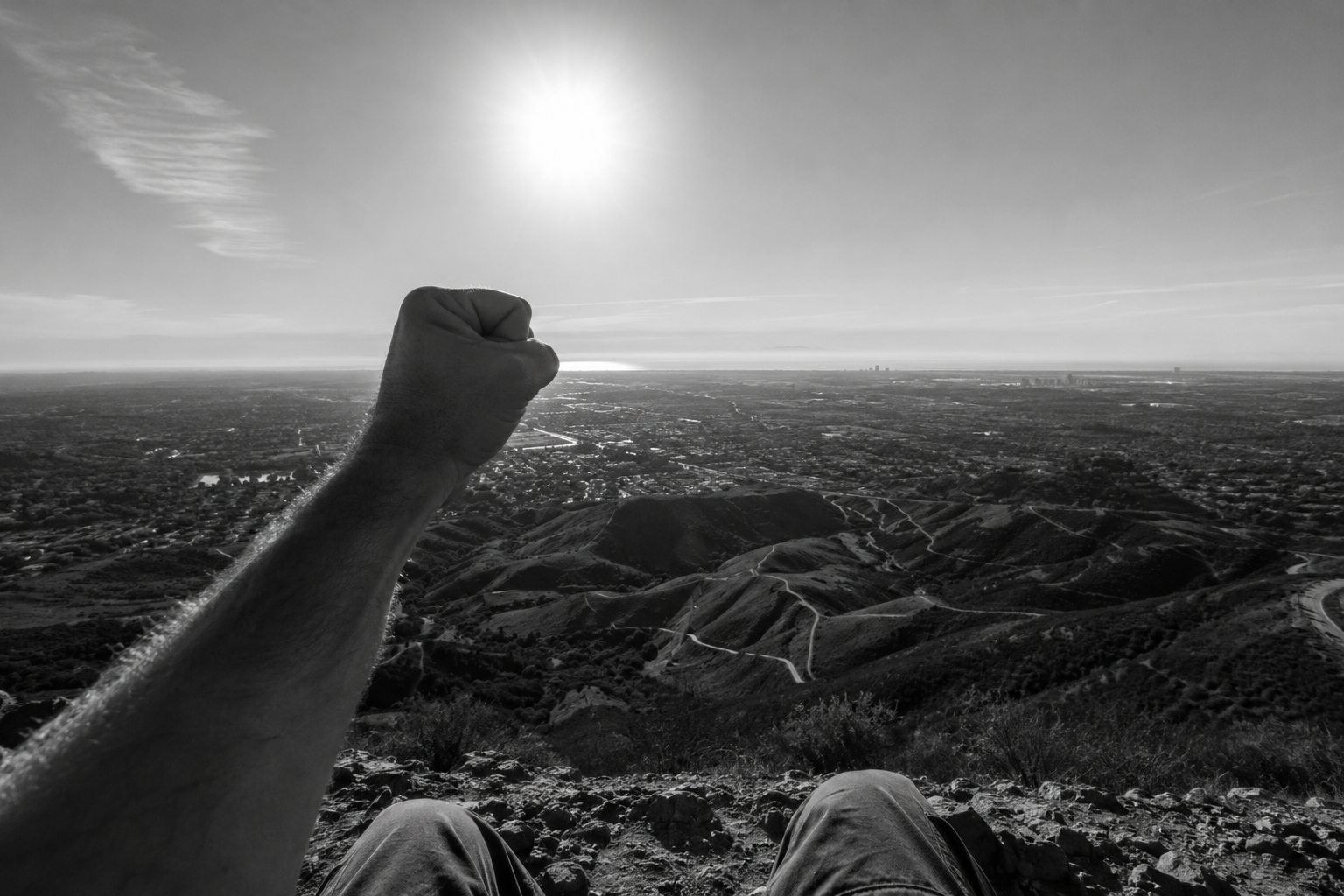 A clenched fist raised toward the sun above rolling hills, black and white